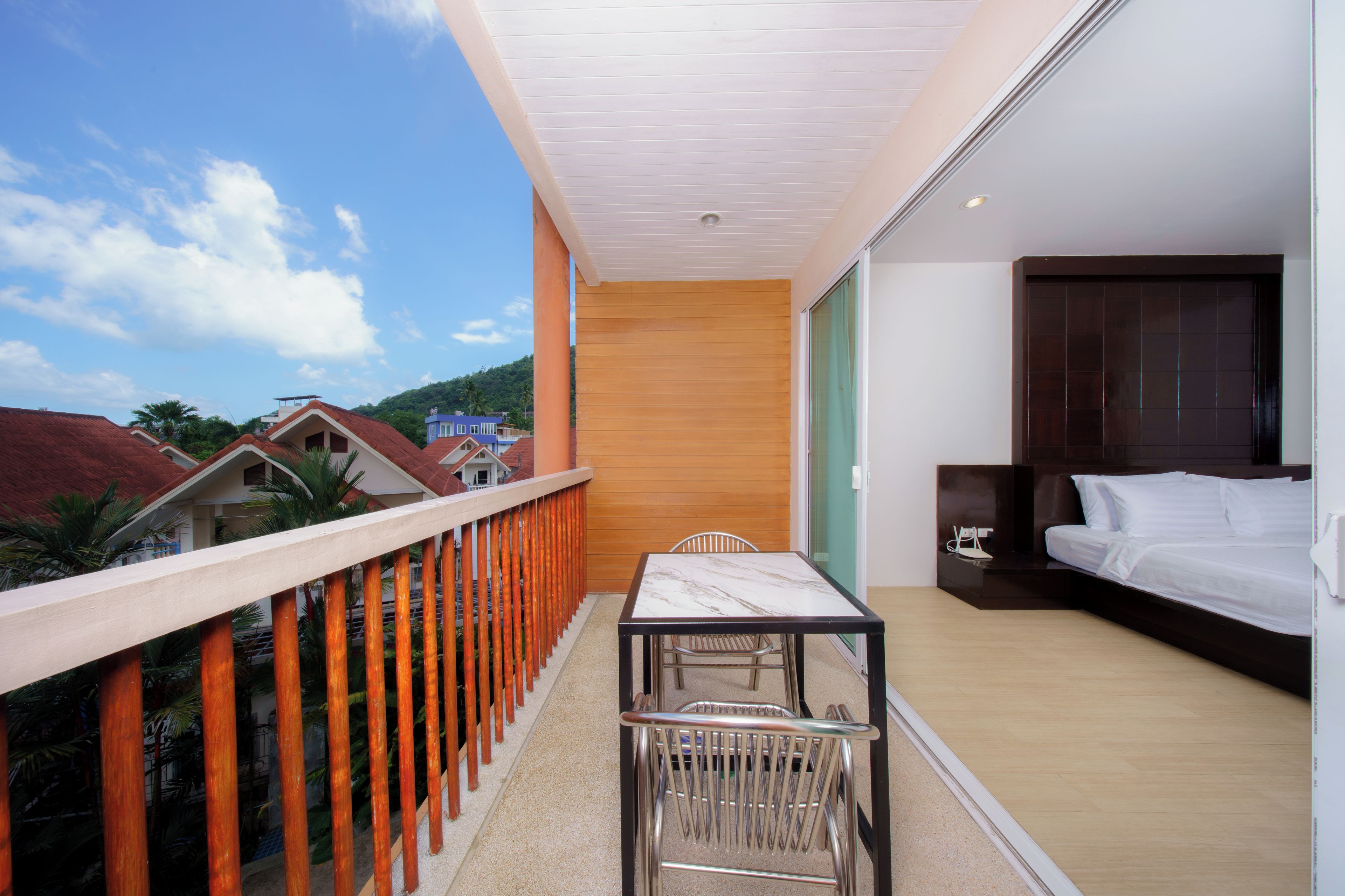 A balcony with a table and chairs, a bed with a headboard, and a view of the surrounding area.