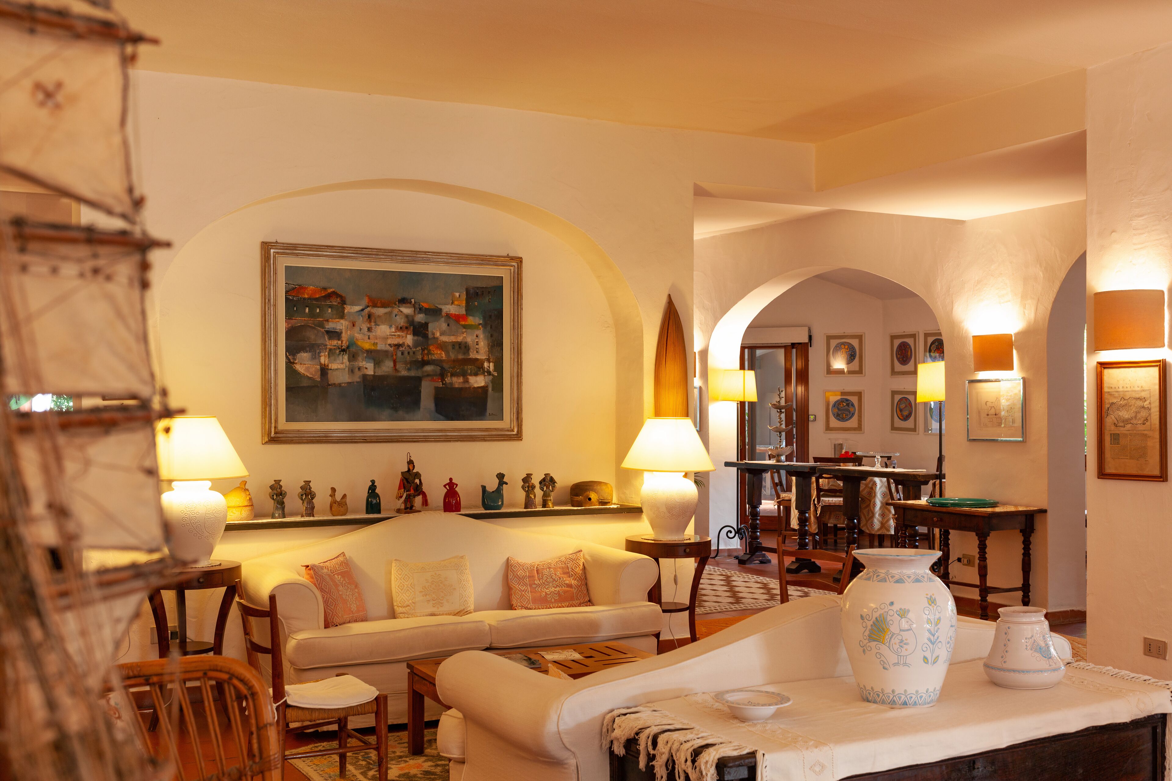 A cozy living room with a sofa, armchairs, and a coffee table. There are decorative items like a vase and figurines on a shelf.