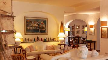 A cozy living room with a sofa, armchairs, and a coffee table. There are decorative items like a vase and figurines on a shelf.