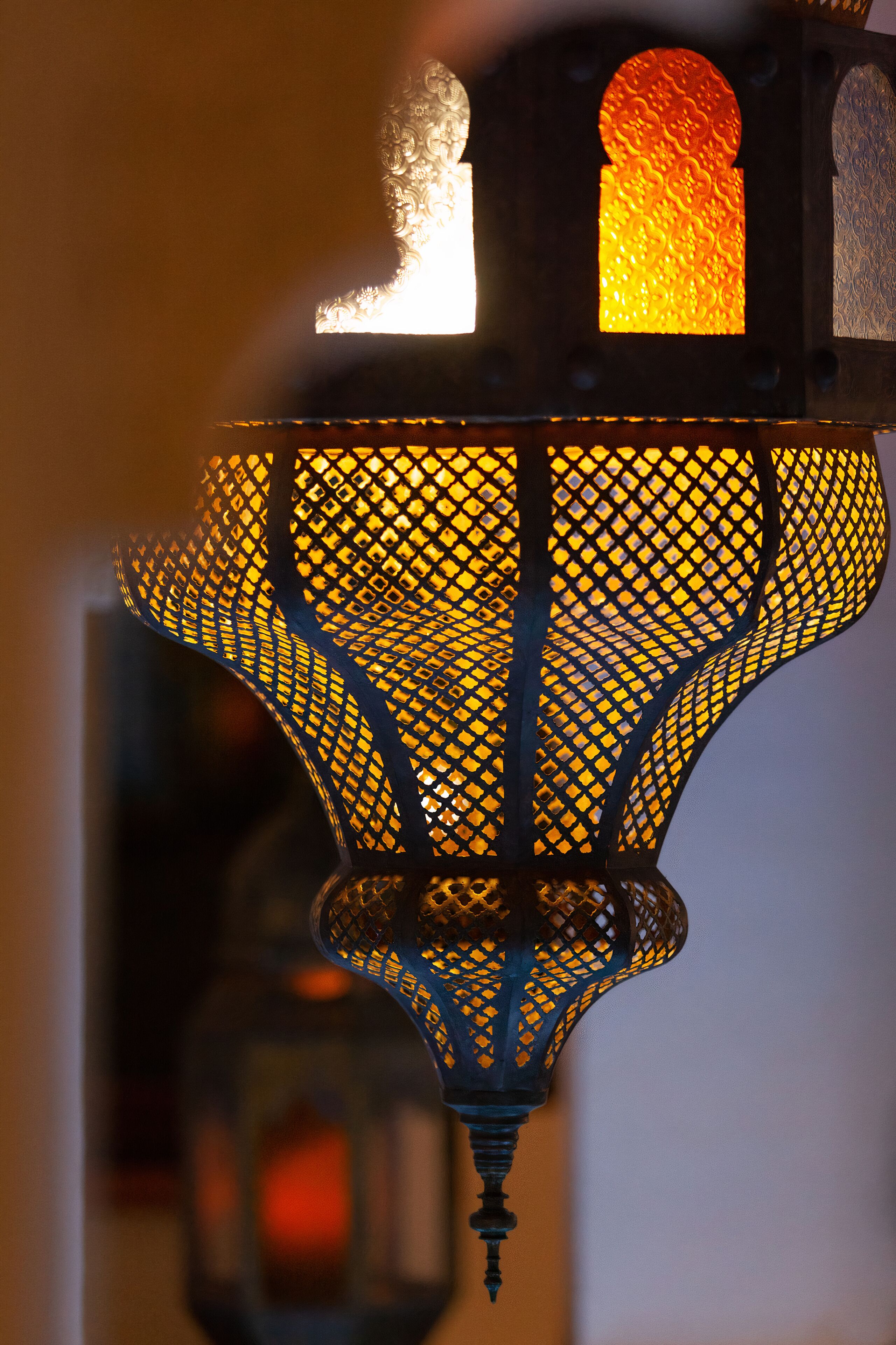 Une vue détaillée d’une lanterne suspendue, ornée de motifs métalliques complexes et dotée d’une source de lumière chaude à l’intérieur.