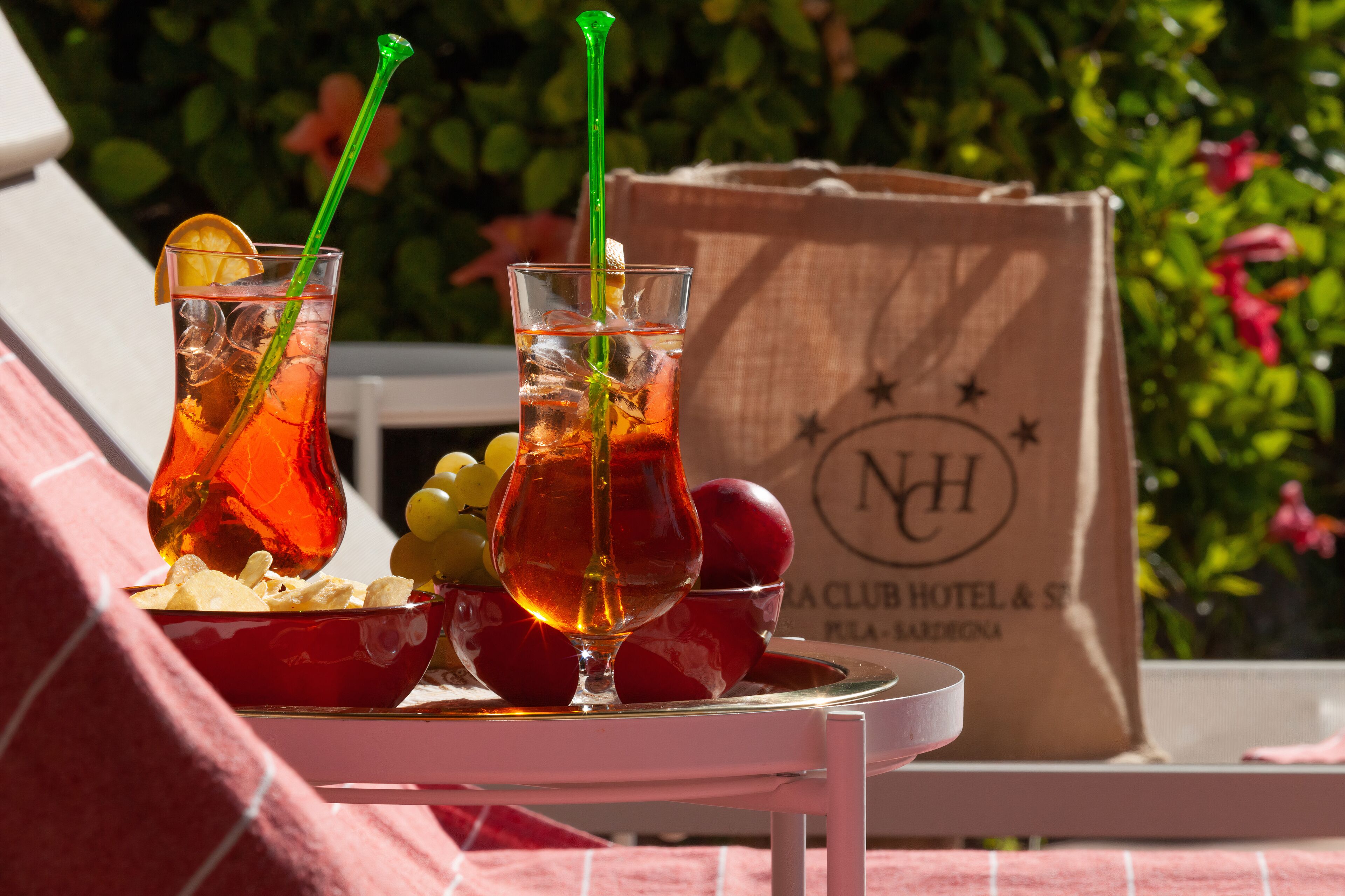 A table with two glasses of iced tea, a bowl of chips, and a bowl of fruit. A hotel bag is visible in the background.