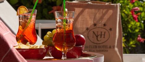 Une table avec deux verres de thé glacé, un bol de chips et un bol de fruits. On aperçoit un sac d’hôtel à l’arrière-plan.