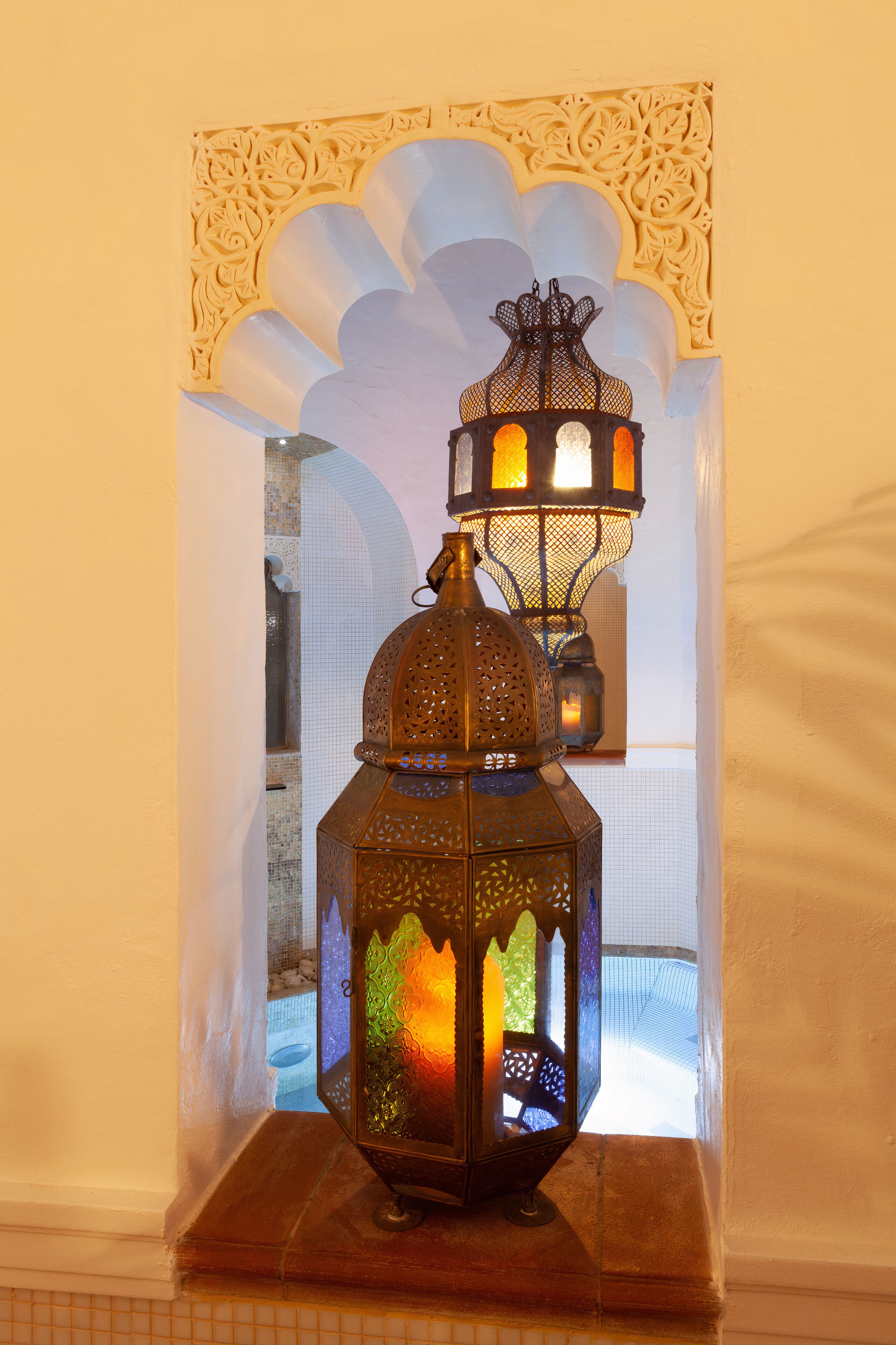 A traditional lantern with intricate designs, placed on a tiled ledge against a wall with ornate architectural details.