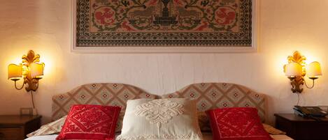 A bed with a patterned headboard, two bedside lamps, and a framed artwork above.