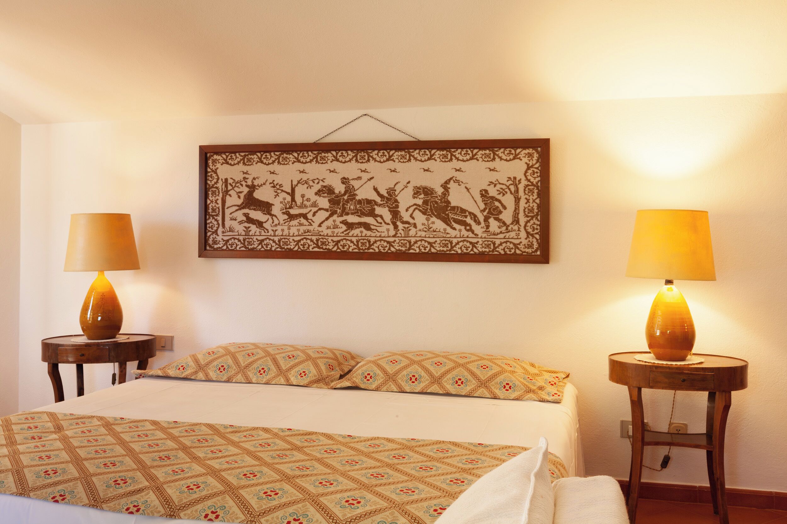 Une chambre à coucher avec un lit, deux lampes de chevet, une décoration murale à motifs et une petite table.