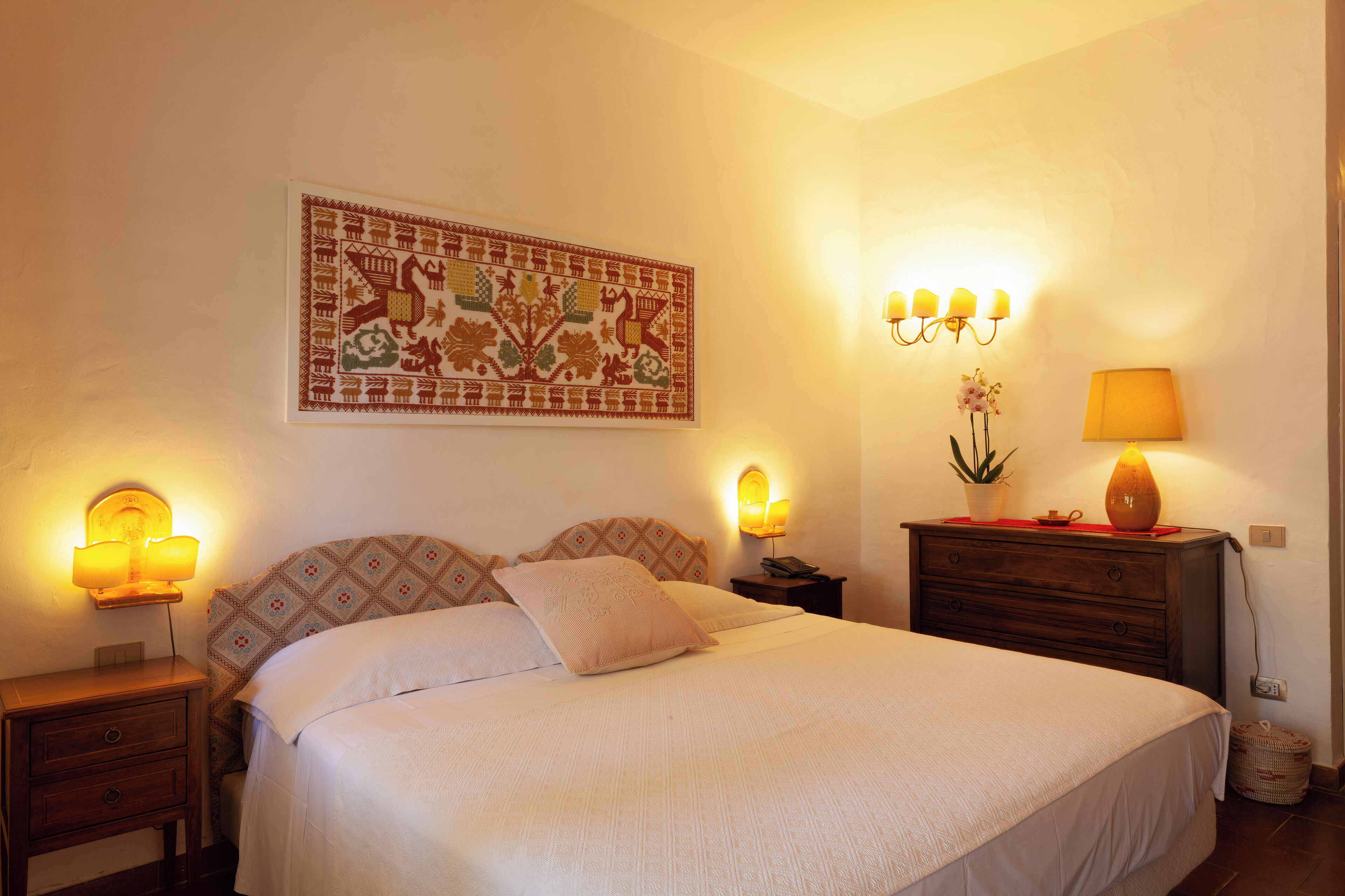 Un lit bien fait, avec une tête de lit à motifs, une tapisserie accrochée au mur et des lampes de chevet.