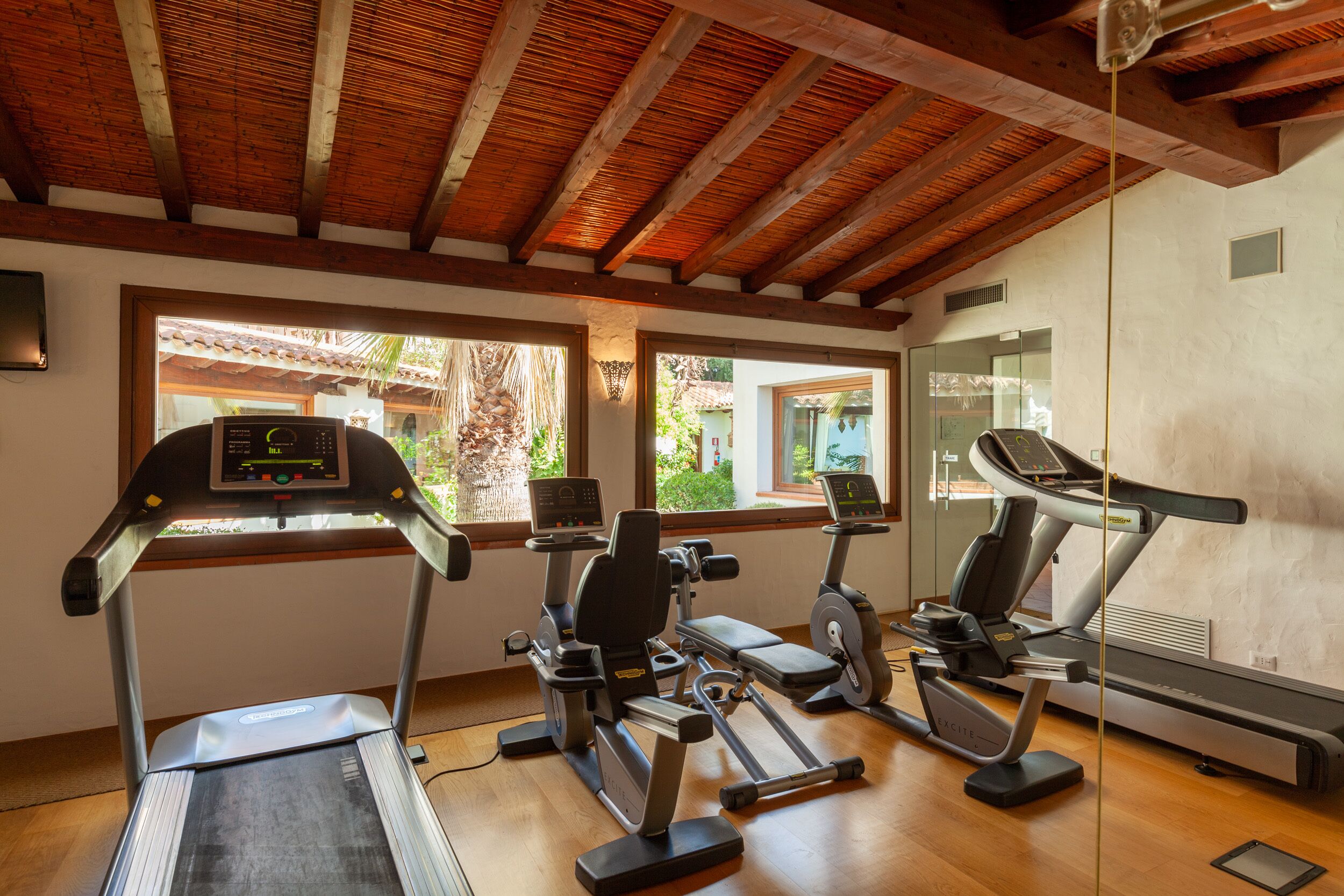 Un gimnasio con cintas de correr, elípticas y una bicicleta estática. Amplias ventanas ofrecen luz natural y vistas al exterior.