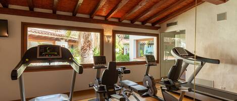 Un gimnasio con cintas de correr, elípticas y una bicicleta estática. Amplias ventanas ofrecen luz natural y vistas al exterior.