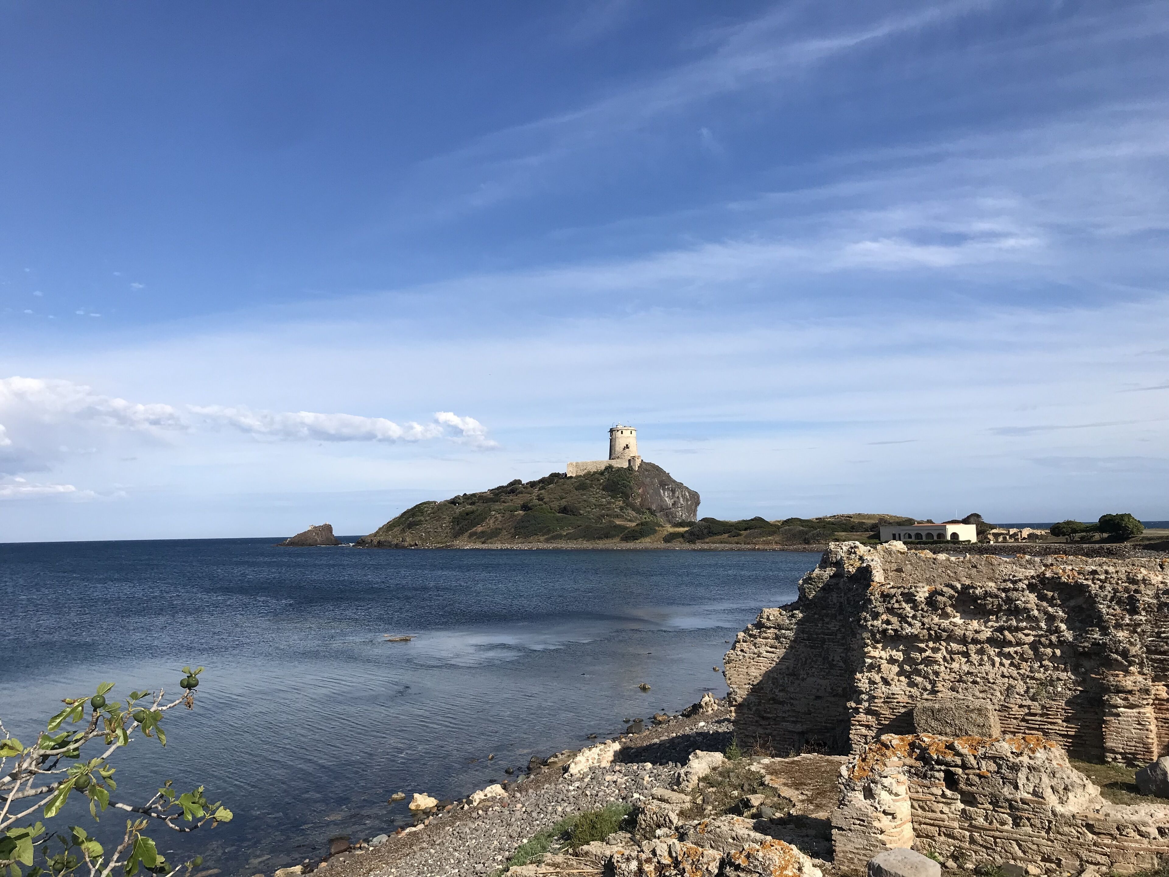 A coastal landscape with a lighthouse on a rocky outcrop, a clear sky, and calm sea.