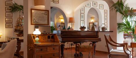 A spacious living room with a grand piano, wooden furniture, and a large map on the wall.
