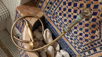 A bathroom with a mosaic floor, a metal hose, and a tiled wall.