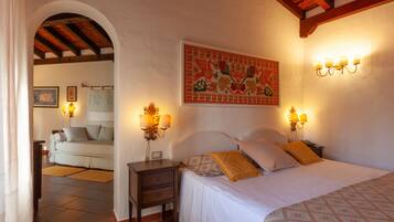 A bedroom with a bed, nightstands, and wall-mounted lamps. There is a painting on the wall and a door leading to another room.