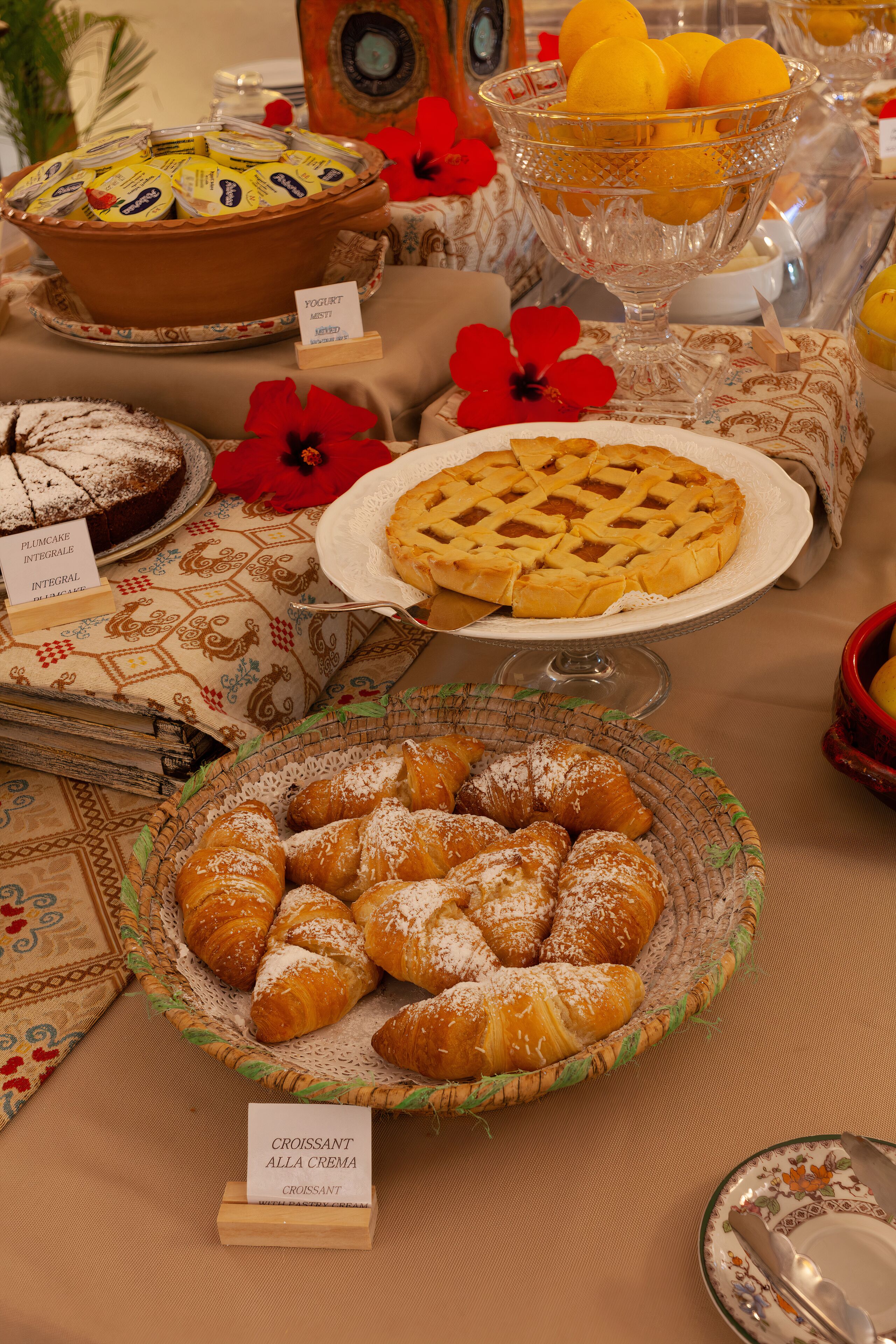 A buffet table with various food items including a pie, croissants, and a bowl of fruit.