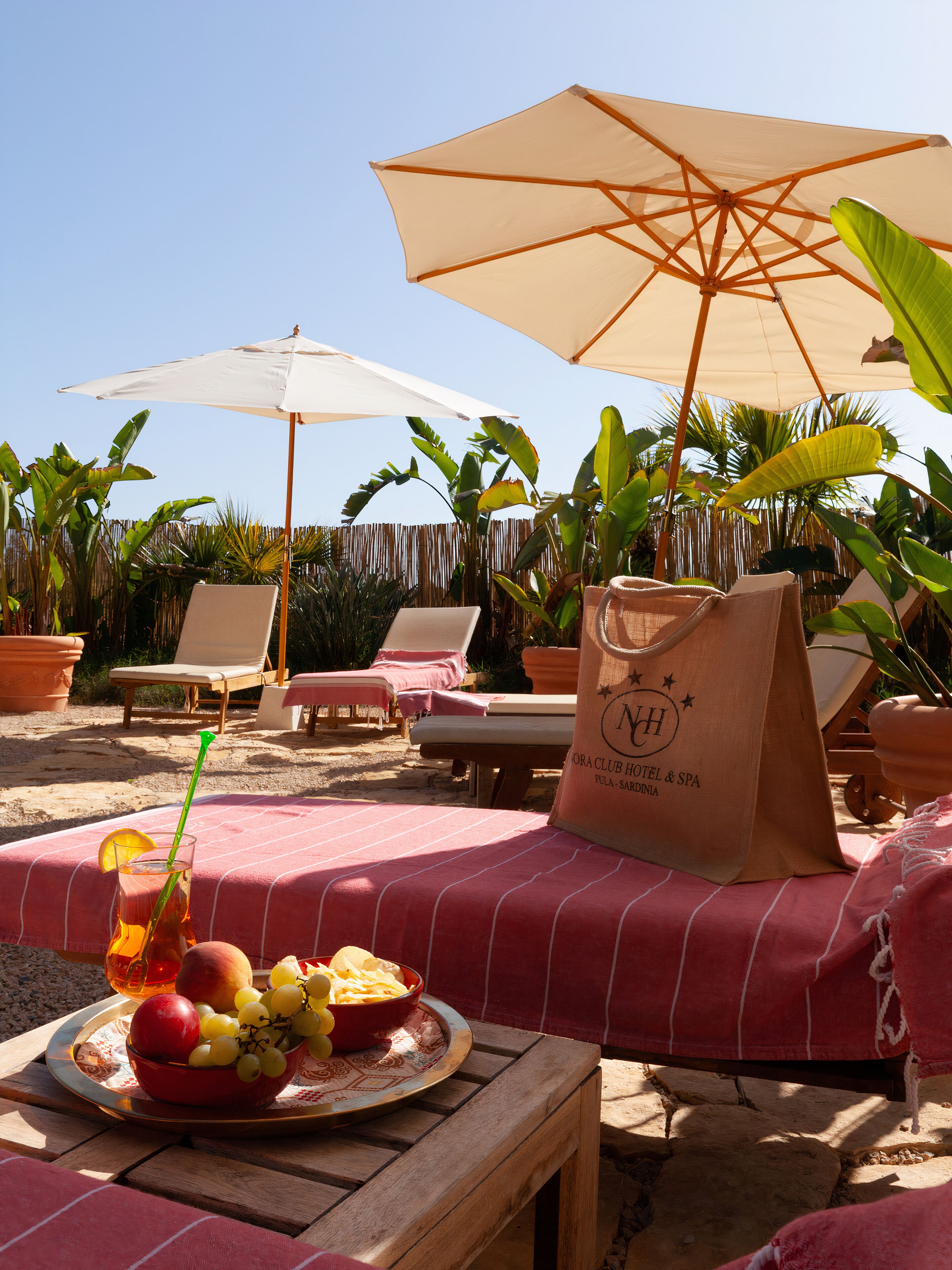 Un área de descanso junto a la playa con tumbonas, una mesa con frutero y sombrillas que dan sombra.