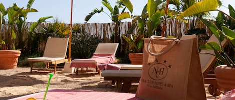 Un área de descanso junto a la playa con tumbonas, una mesa con frutero y sombrillas que dan sombra.