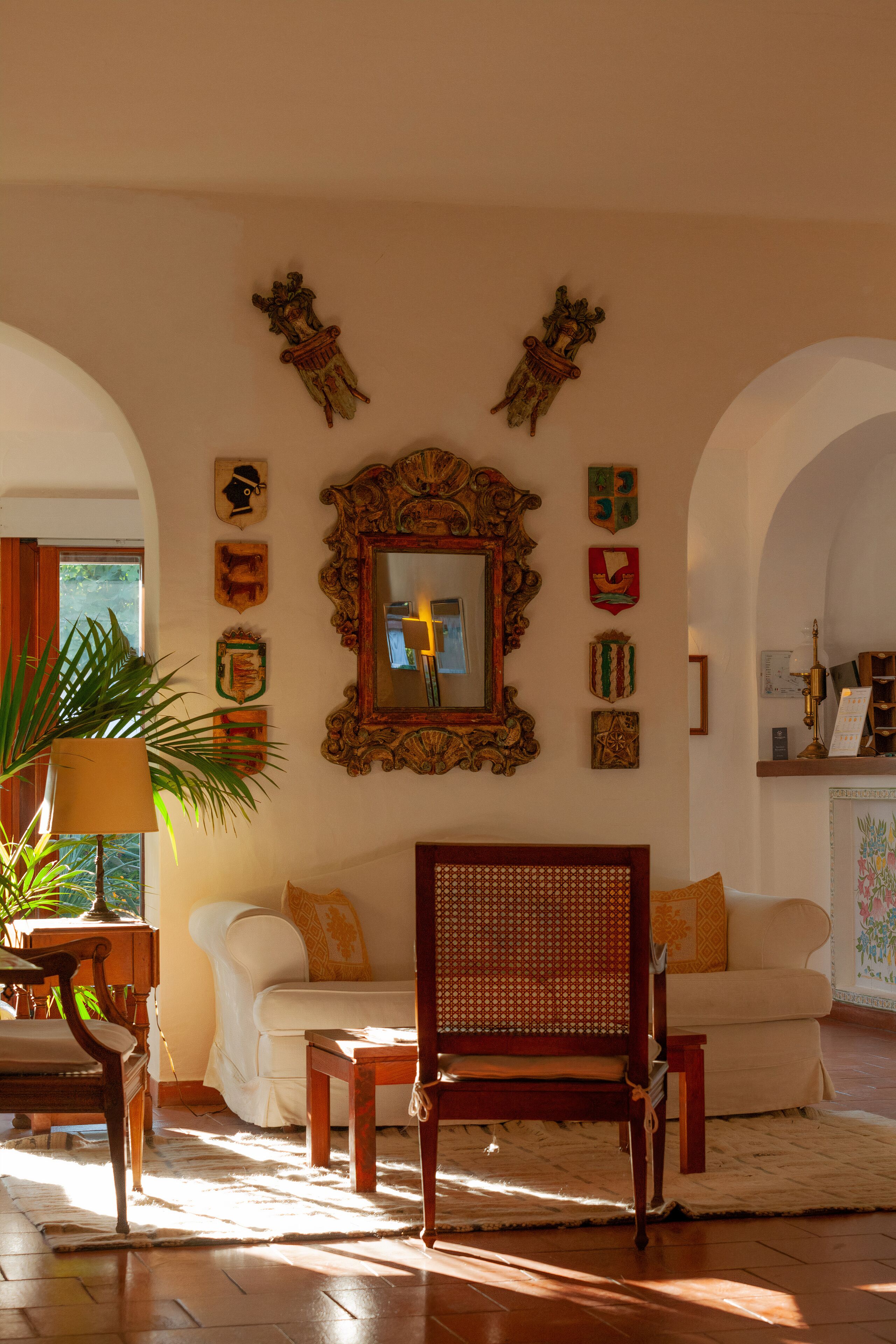 A well-lit living room with a large mirror, two white sofas, a wooden chair, and various wall decorations.