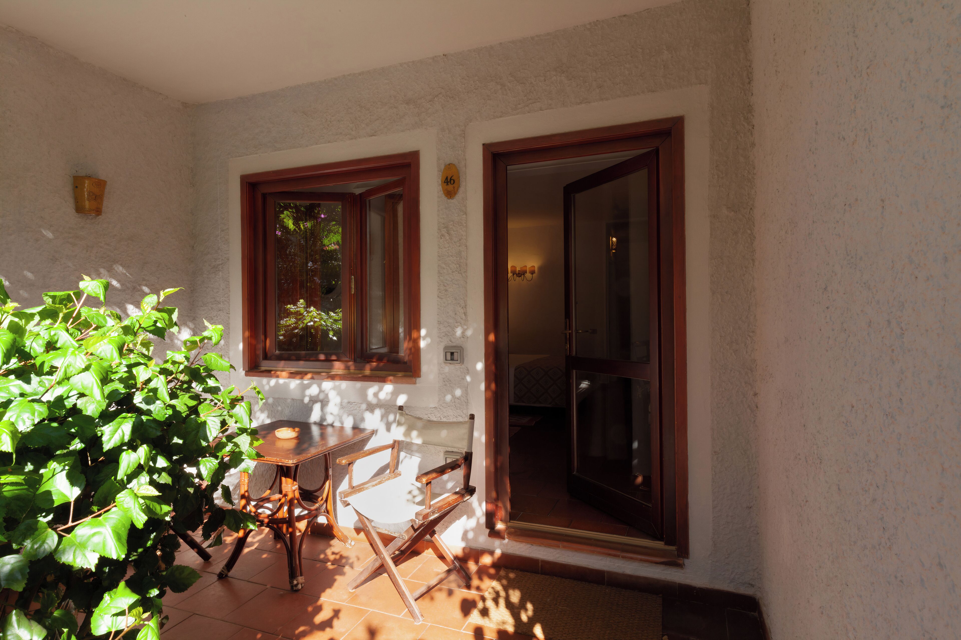 A sunlit patio with a table and chairs, a potted plant, and a door leading to an interior space.