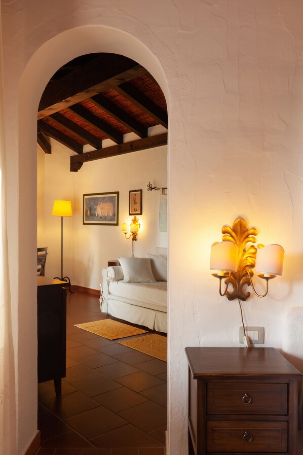 A cozy room with a wooden ceiling, a white sofa, a small table, and a wall-mounted lamp.