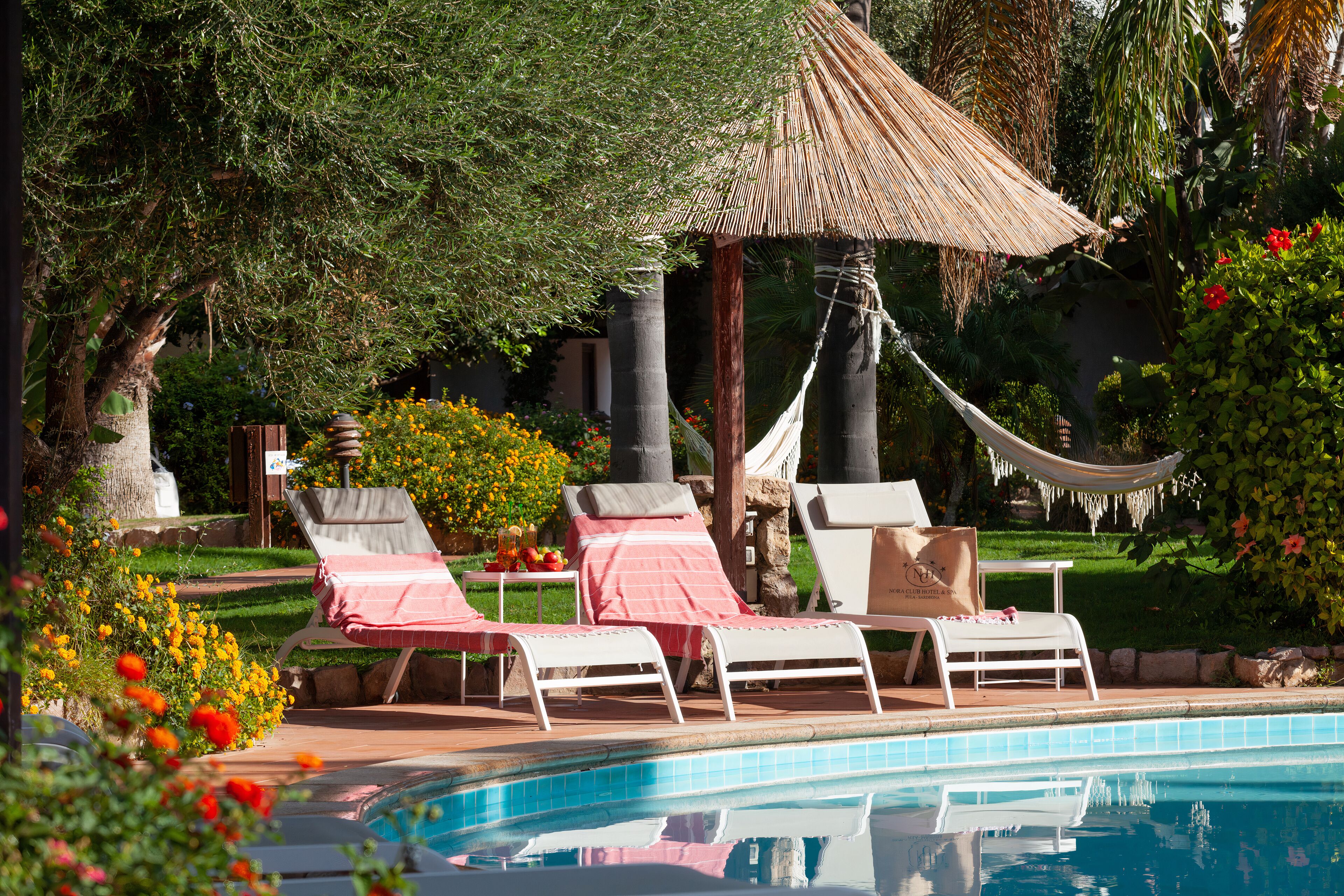 A pool area with lounge chairs, a hammock, and a thatched-roof structure.