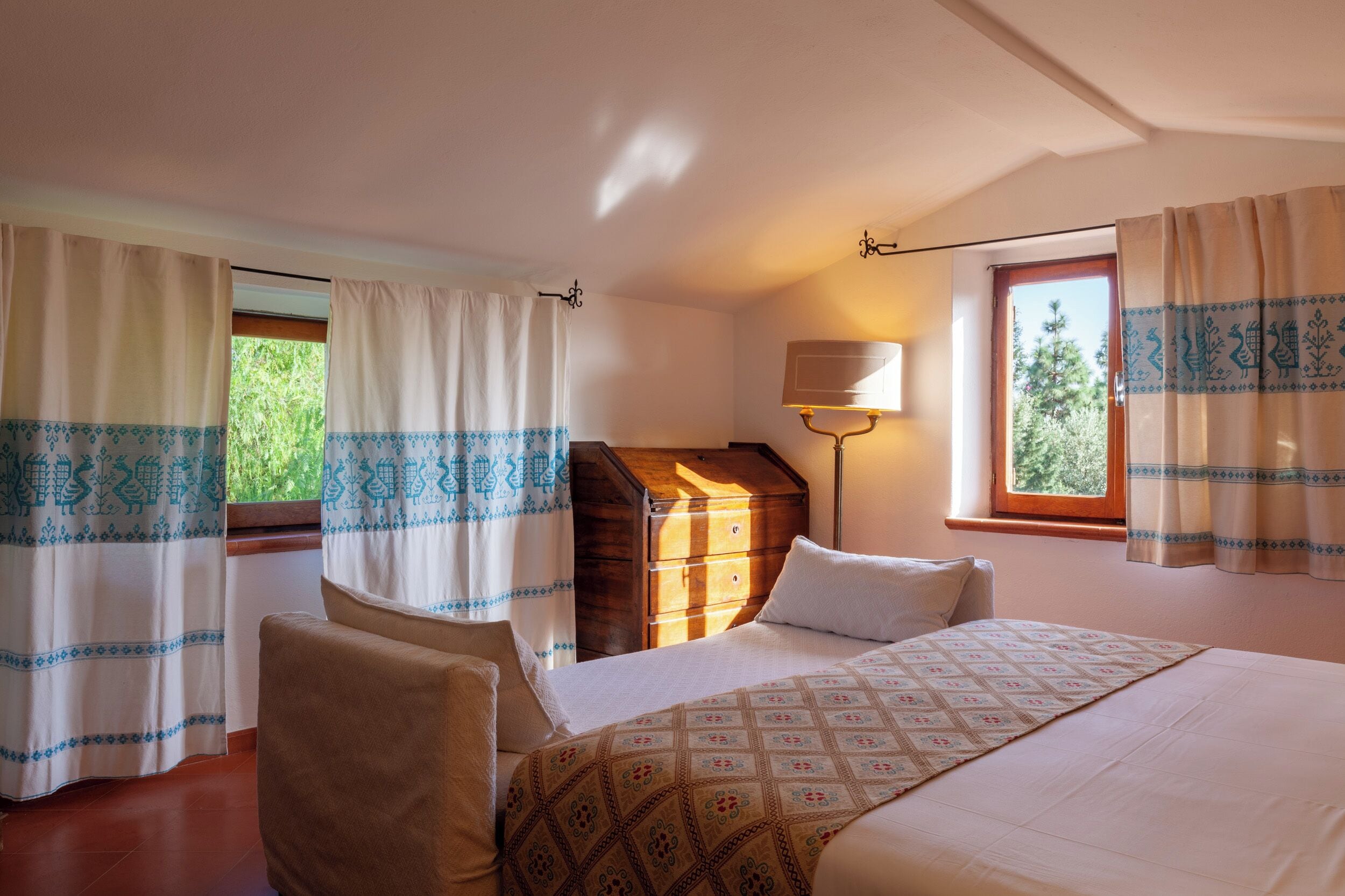 Une chambre à coucher avec un lit, une commode en bois, une lampe et des rideaux.