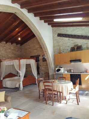 A cozy room with a bed, a dining table with chairs, a kitchen area, and a stone wall.
