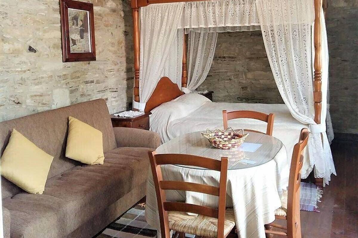 Ein rustikales Schlafzimmer mit Himmelbett, einer Holzbank, einem kleinen Tisch und einer Steinwand.