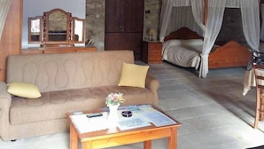 A rustic room with a stone wall, a wooden ceiling, a sofa, a bed with a canopy, and a small table with a vase of flowers.