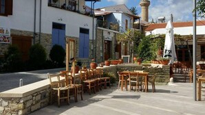 An outdoor seating area with stone walls and wooden furniture, a mosque with a minaret, and a clear sky.