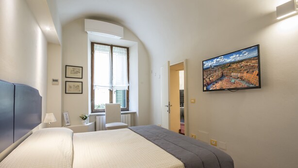 Ett hotellrum med en säng, ett skrivbord, en stol, ett fönster och en tv på väggen.