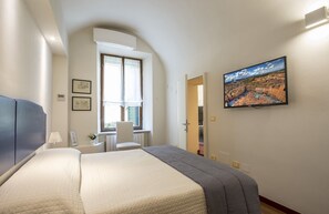 A hotel room with a bed, a desk, a chair, a window, and a TV on the wall. - Quattro Cantoni (Siena)
