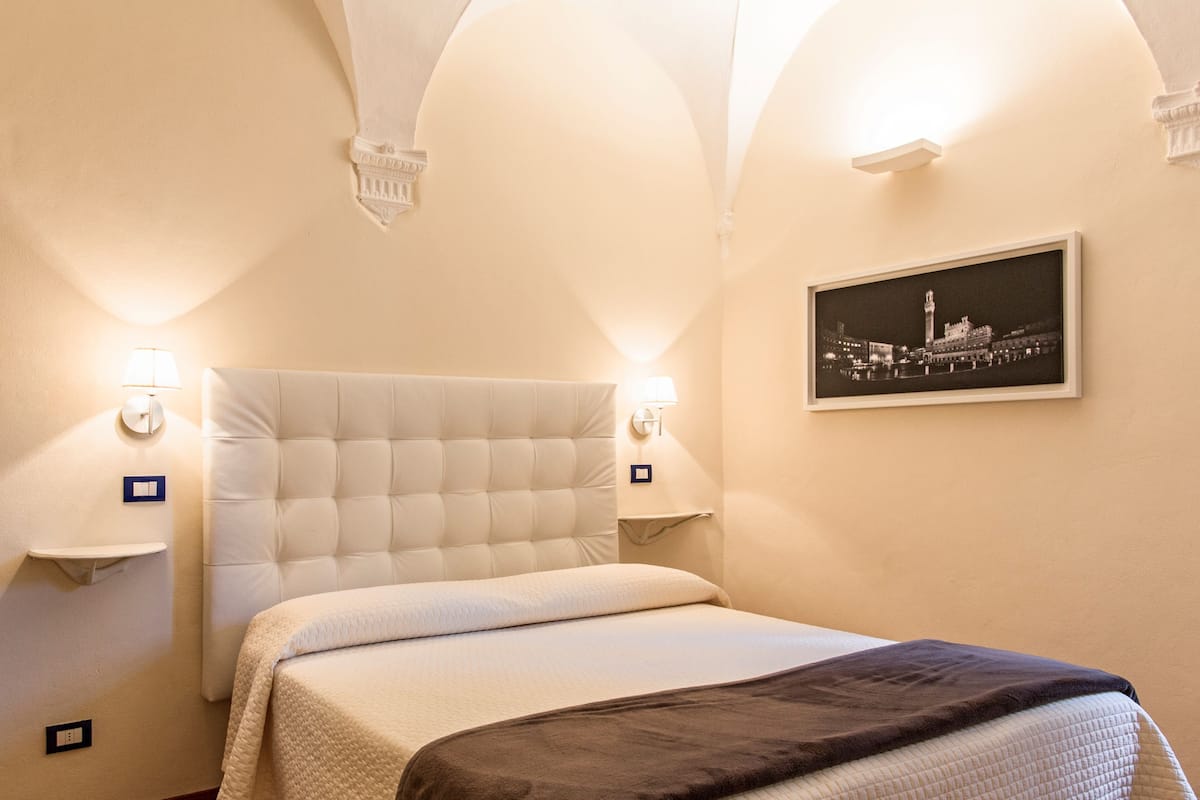 A hotel room with a large bed, two bedside lamps, a framed picture on the wall, and a small table with a lamp.