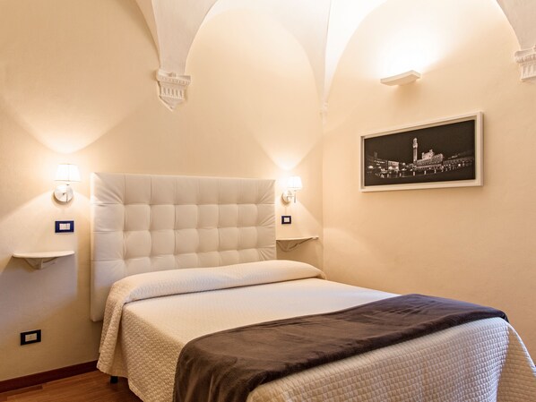 Habitación de hotel con una cama grande, dos lámparas de noche, un cuadro en la pared y una mesita con lámpara.