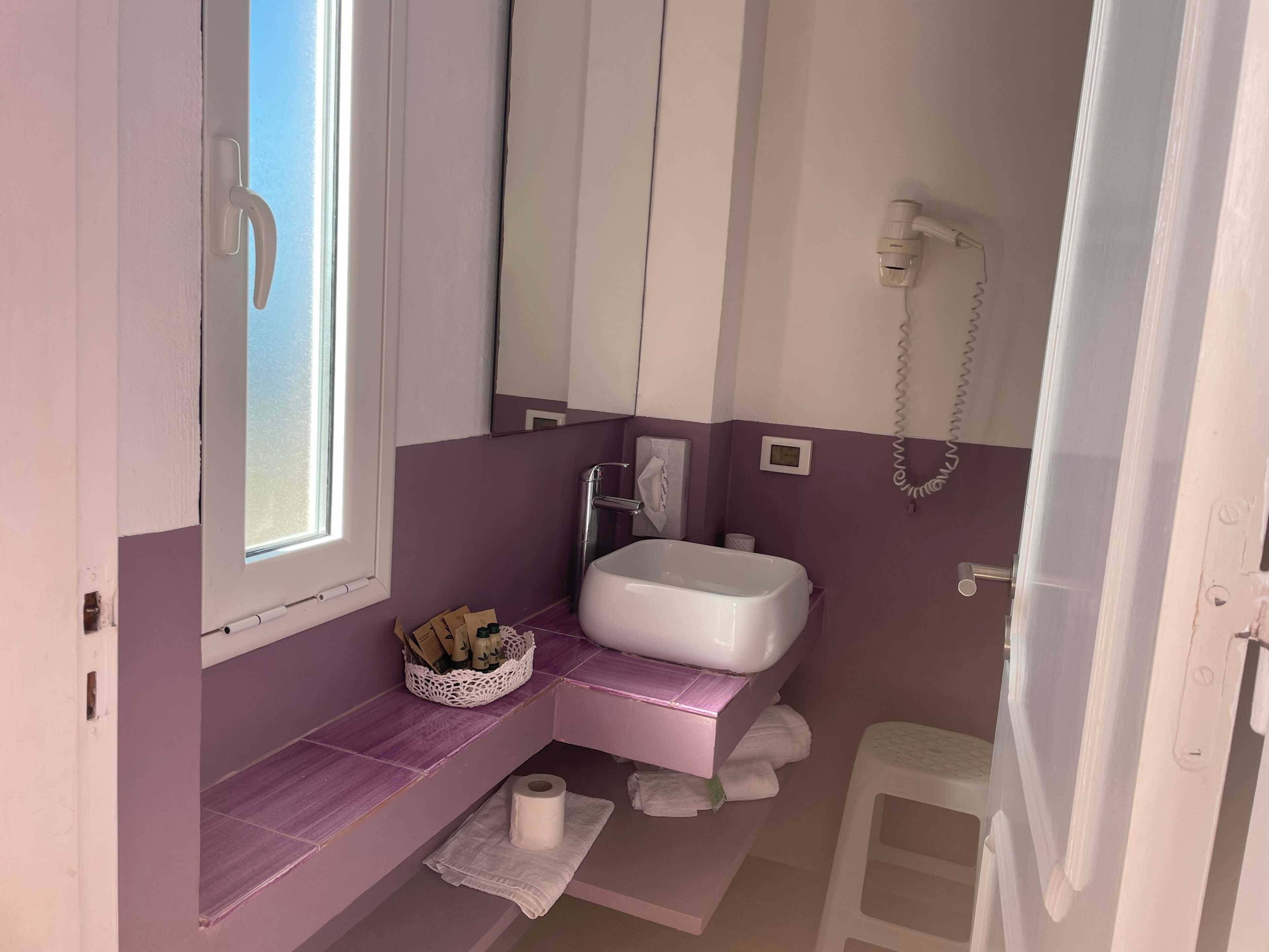 A bathroom with a window, a sink, a mirror, a towel rack, and a toilet.