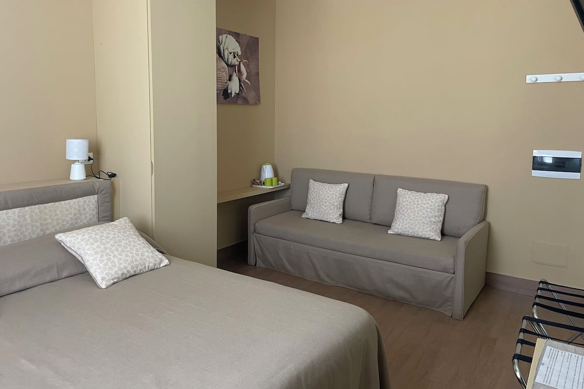 Ein Hotelzimmer mit Bett, Sofa, Lampe, einem kleinen Tisch mit Tassen und einem Gemälde an der Wand.