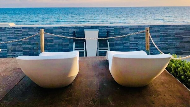 A wooden deck with two white chairs facing a stone wall and a view of the ocean.