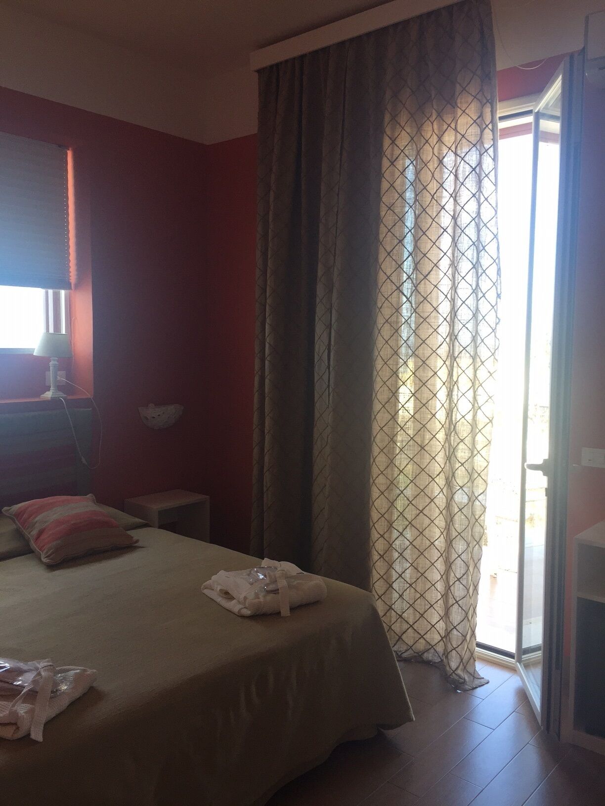 Una habitación de hotel con cama, mesita de noche, lámpara y ventana con cortinas.