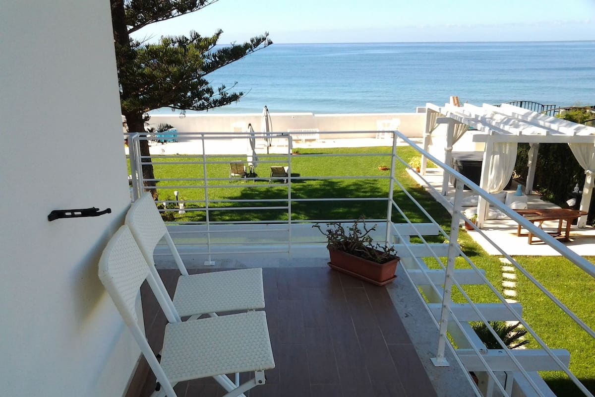 Ein Balkon mit weißem Stuhl, einer Topfpflanze und Blick auf den Ozean.