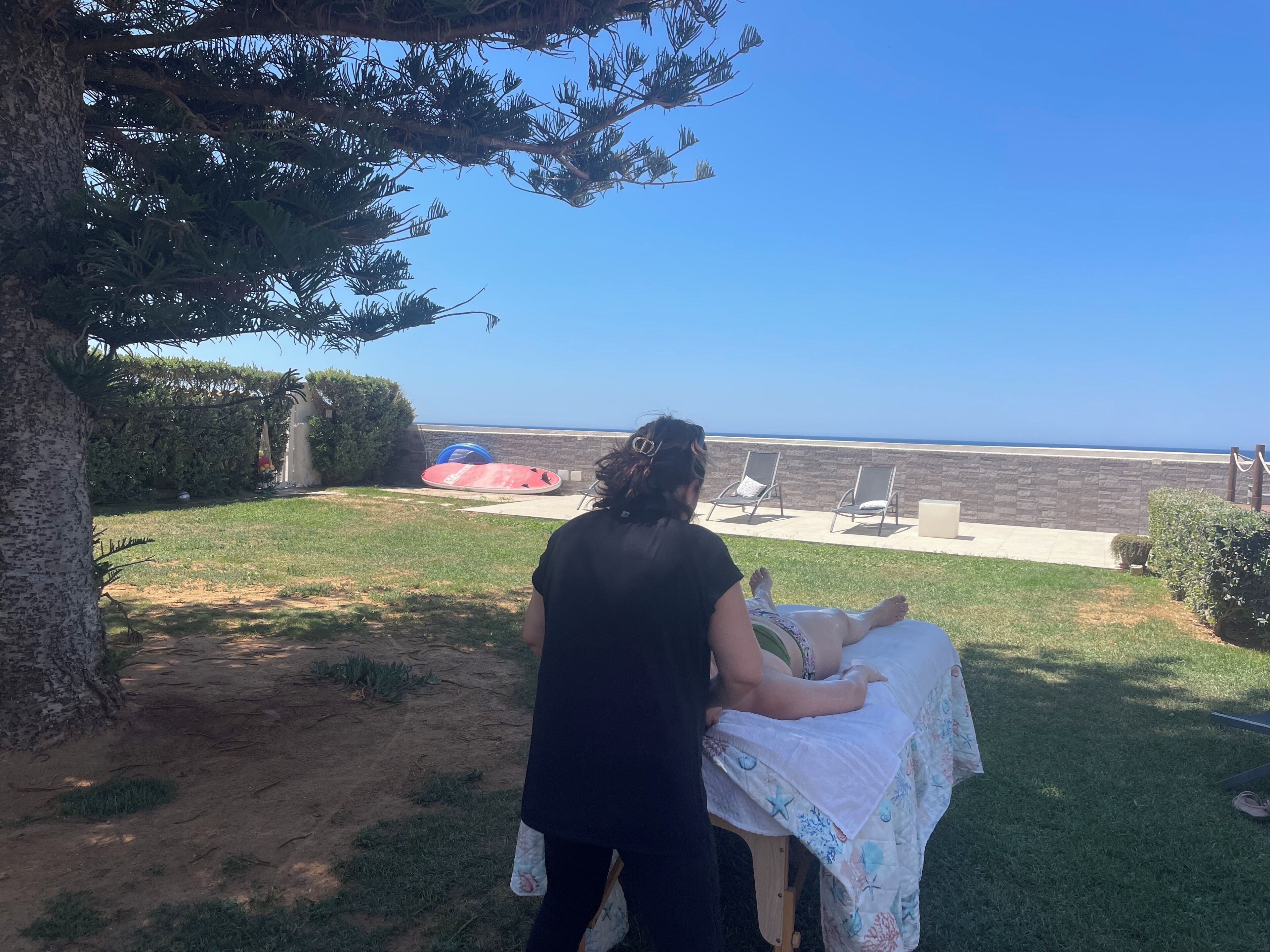 Une personne s’occupe d’un enfant assis sur une chaise longue, enveloppé dans une couverture, et ils sont tous les deux face à une plage et à d’autres chaises.