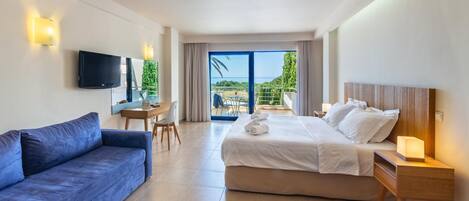 Habitación de hotel con cama, sofá, televisión, escritorio y balcón con vistas.
