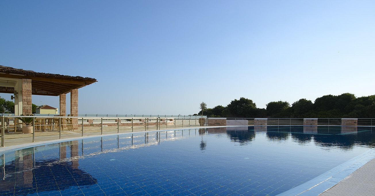 Una piscina con solárium empedrado y una zona de estar cubierta.