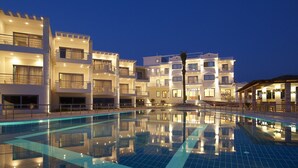 Un hotel con varios pisos, piscina y fachada iluminada al anochecer.