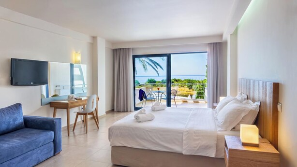 Habitación de hotel con cama, escritorio, silla, televisión y balcón con vista al mar.