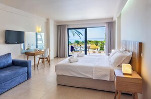 Habitación de hotel con cama, escritorio, silla, televisión y balcón con vista al mar.