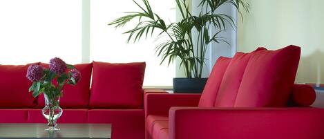 A modern living room with red sofas, a glass coffee table, and a potted plant.
