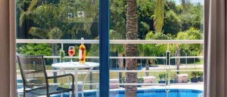 A hotel room with a balcony overlooking a swimming pool and lush greenery.