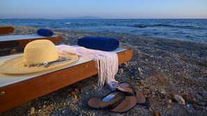Un paisaje playero con un banco de madera, un sombrero de paja, una toalla enrollada y sandalias.