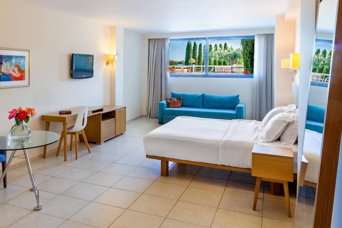 A hotel room with a bed, a desk, a chair, a sofa, and a TV.