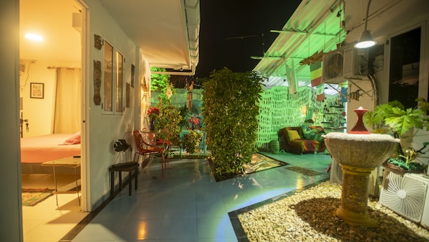 A well-lit indoor space with a bed, chairs, and a small table. There are plants and a decorative fountain. - Posada Nativa Lizard House (San Andrés)