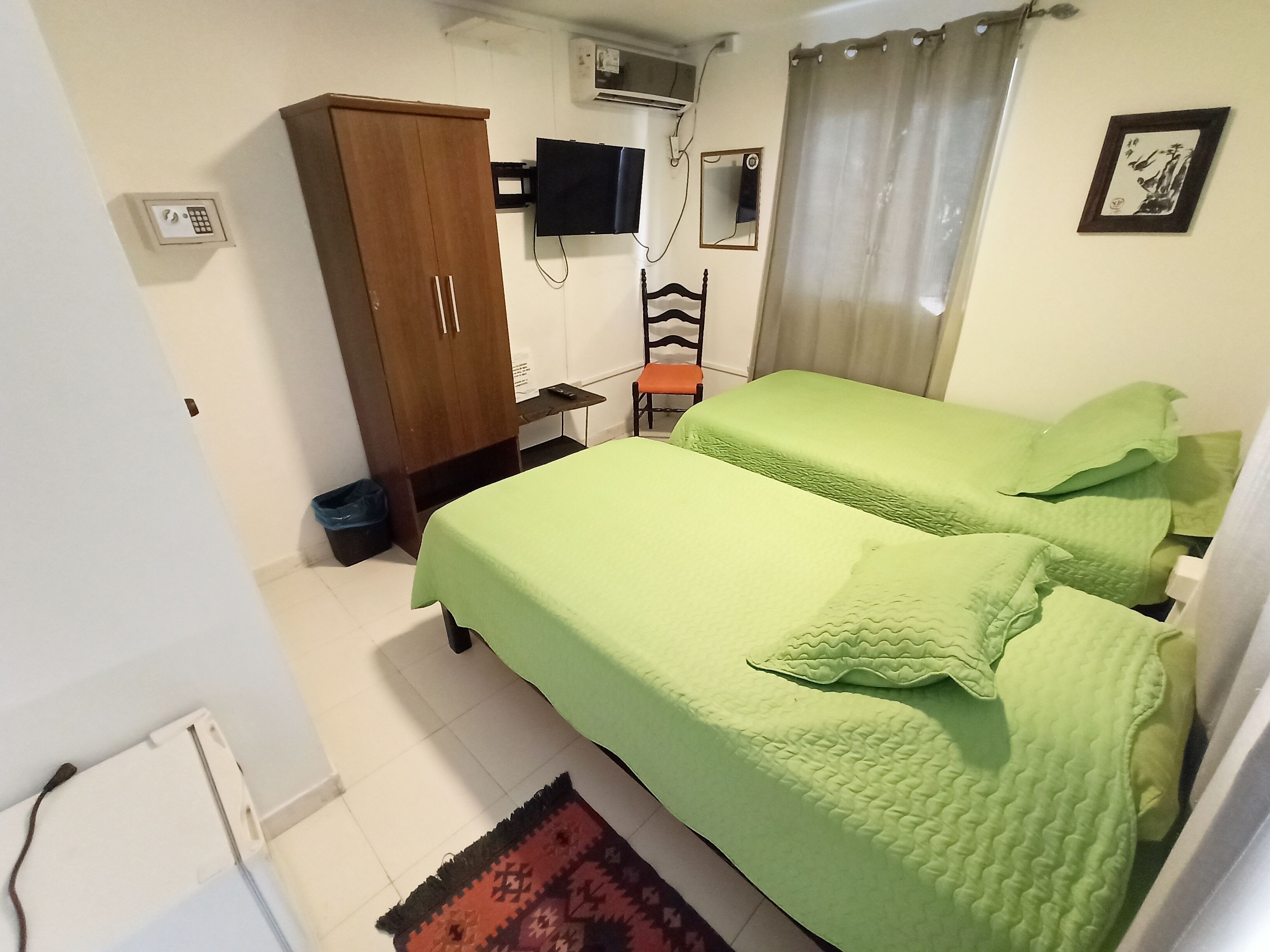 Una habitación con dos camas, un armario, un escritorio con silla, un televisor y un espejo.
