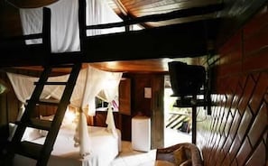 A cabin with a loft bed, a small table, and a window with curtains.